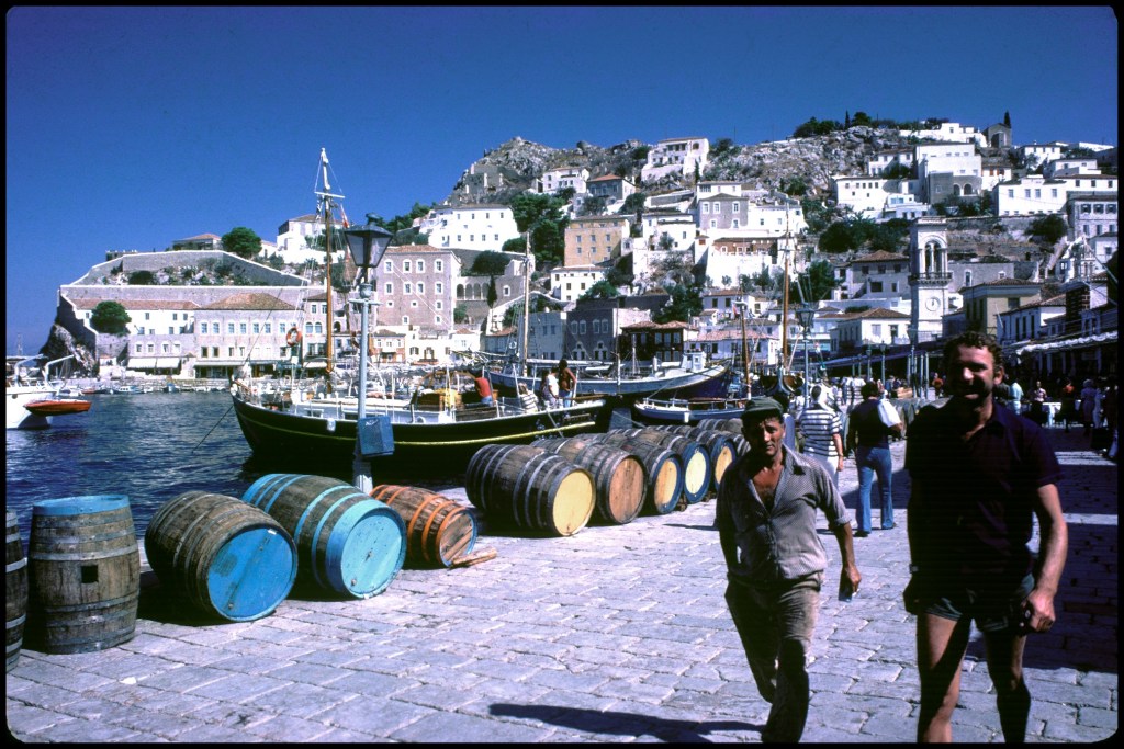 Men walk past barrels on Greek Isle